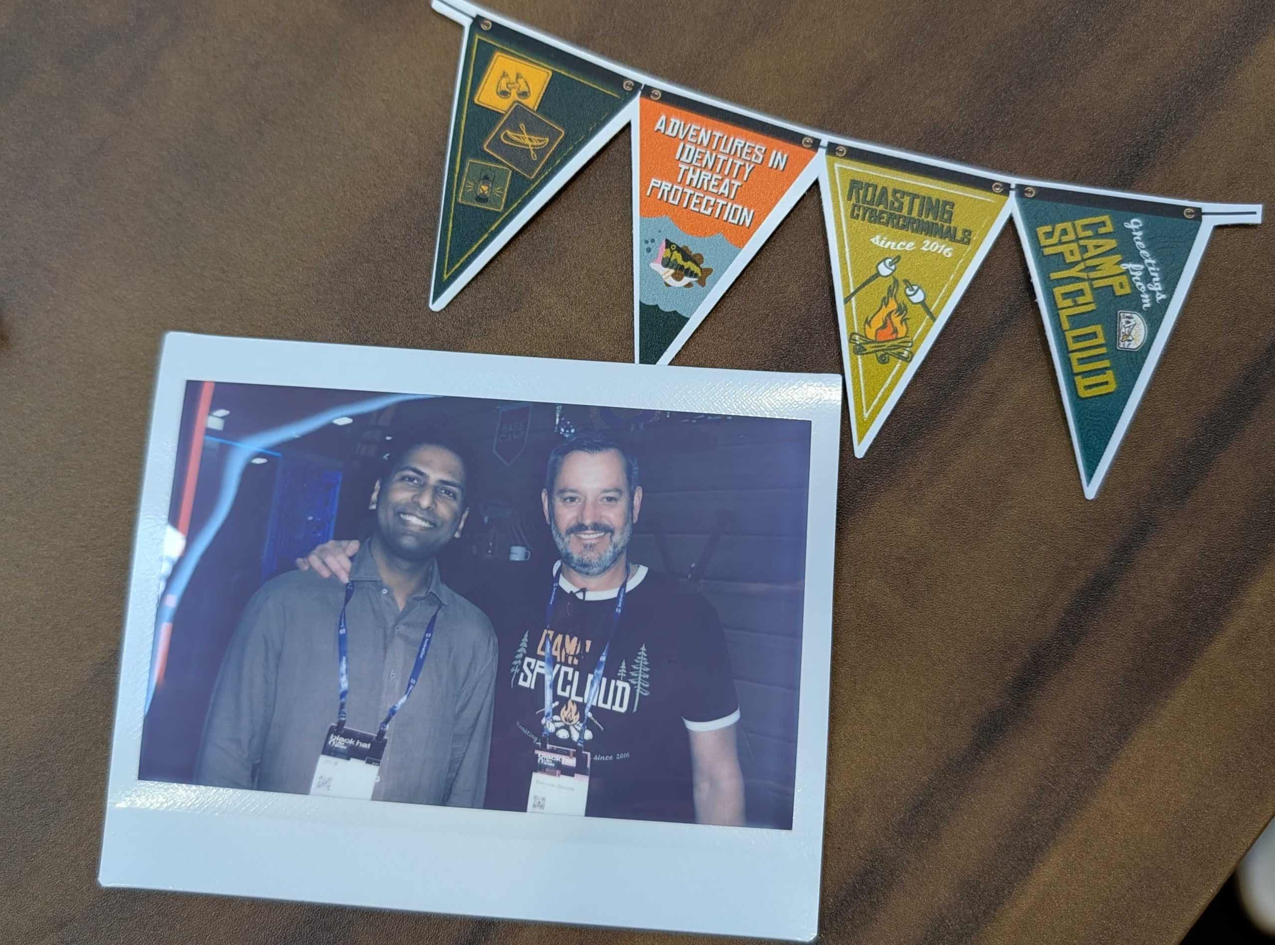 Two men smiling at a cybersecurity event with badges and a banner.