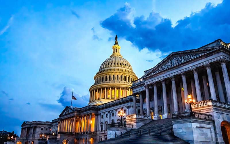 U.S. Capitol with illuminated columns and dome at sunset.