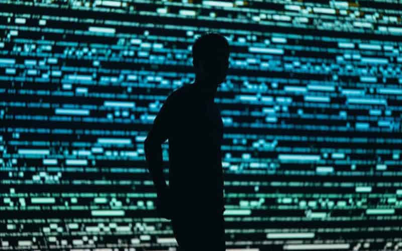 Silhouette of a person in front of digital data streams representing cybersecurity risks.