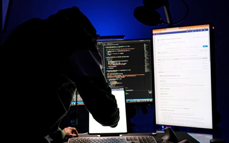 Person working on multiple screens with code and email in a dark room.